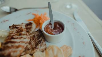 A plate with grilled meat, a small bowl of sauce, and some vegetables.