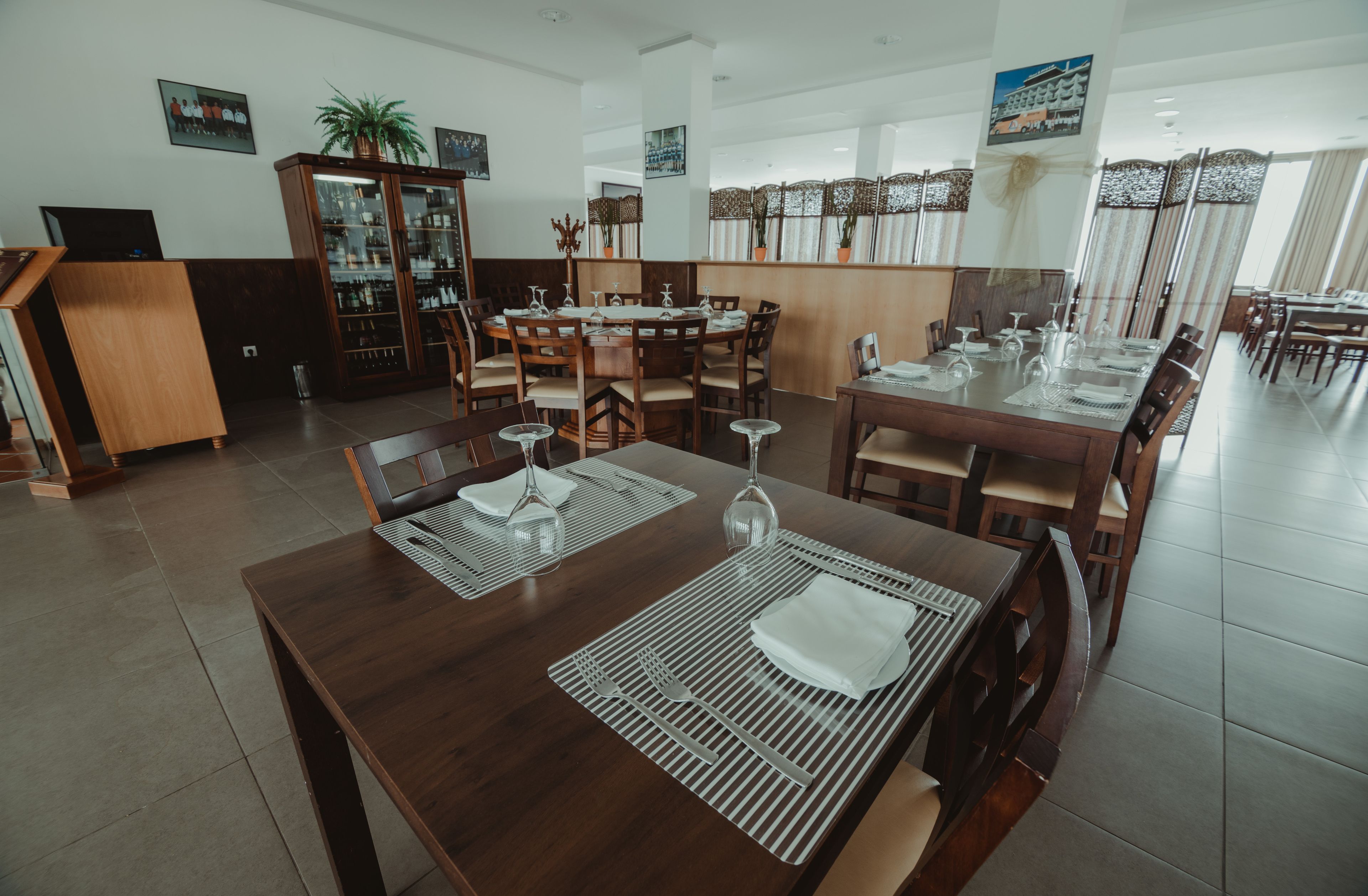 A dining area with wooden tables and chairs, a glass cabinet, and a decorative plant.