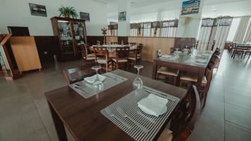 A dining area with wooden tables and chairs, a glass cabinet, and a decorative plant.