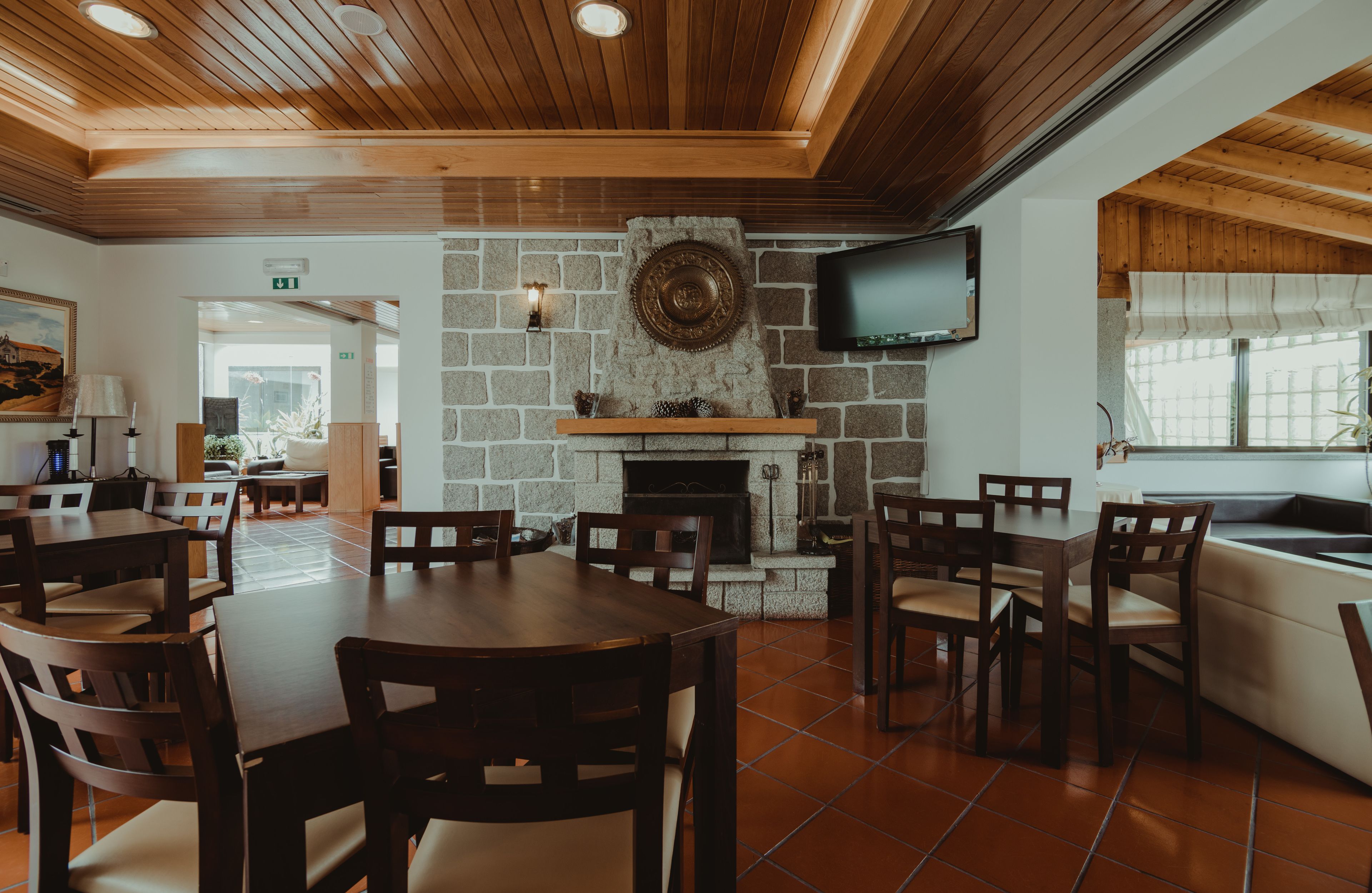 Een restaurant met houten plafond, stenen muur, open haard en een aan de muur bevestigde televisie.