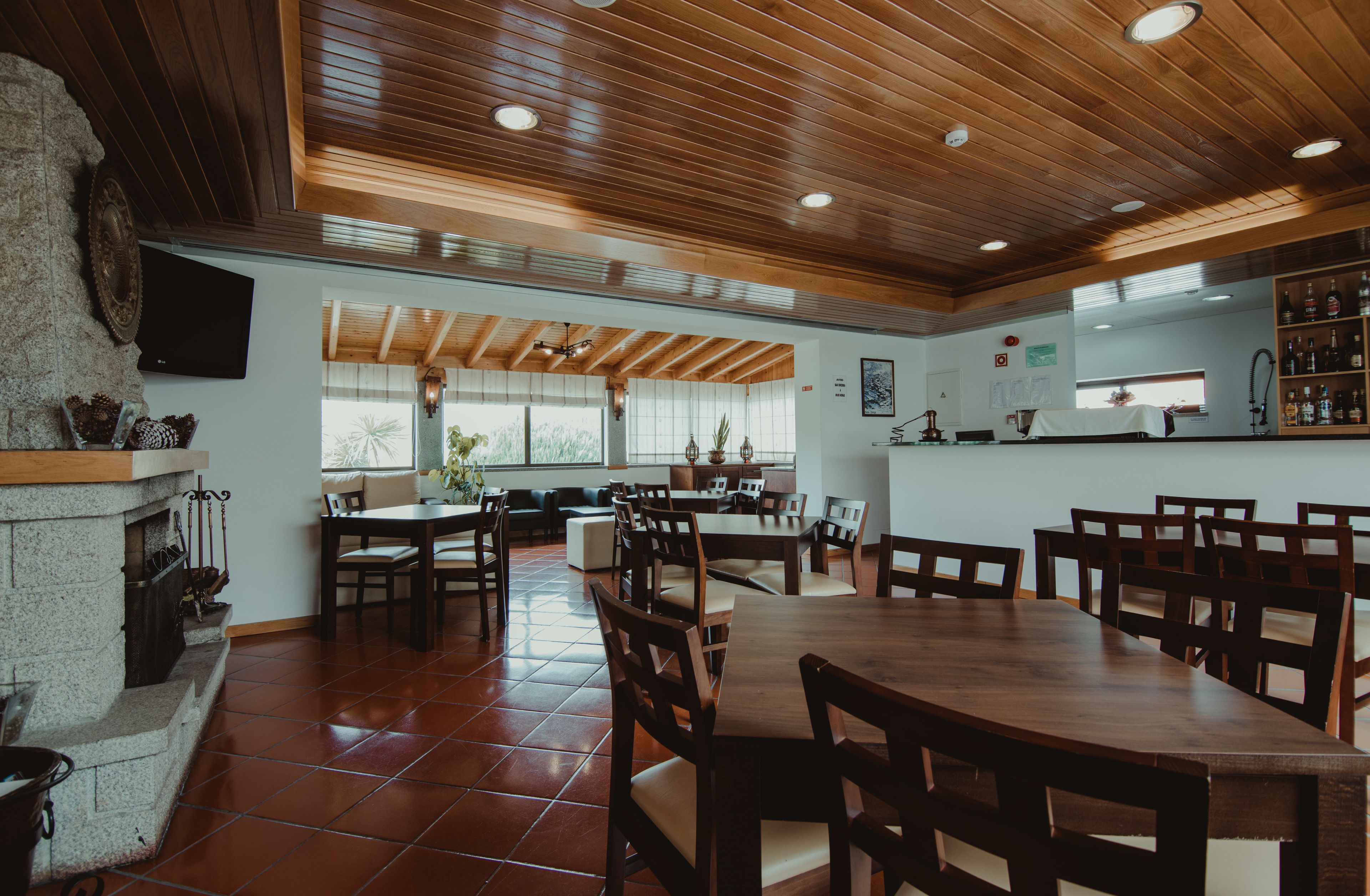 A spacious dining area with wooden tables and chairs, a stone fireplace, and a kitchen area with a bar.