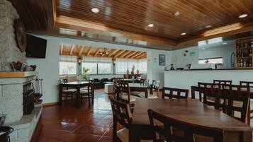 A spacious dining area with wooden tables and chairs, a stone fireplace, and a kitchen area with a bar.