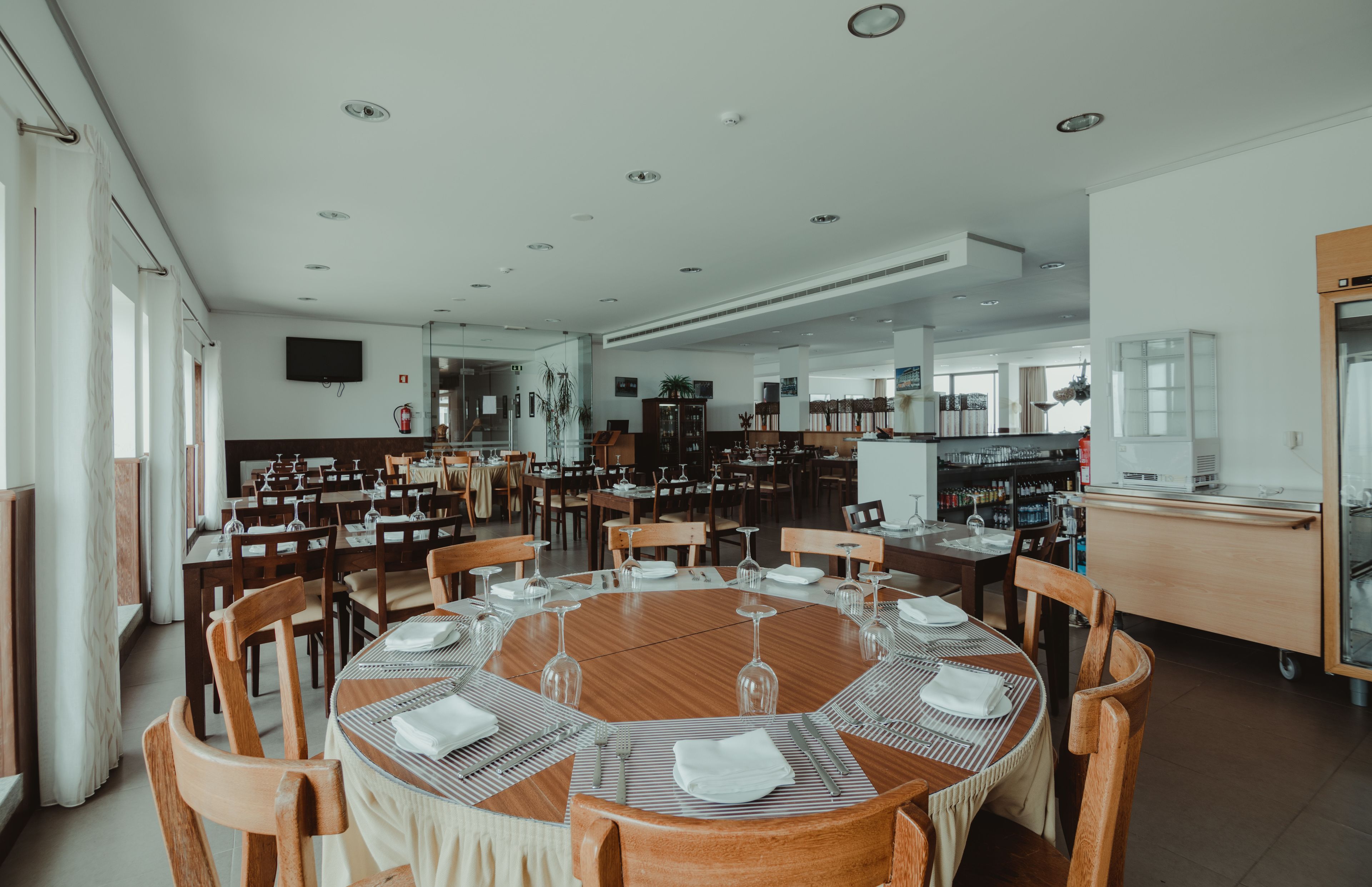 A spacious dining area with multiple round tables set for dining, surrounded by wooden chairs.
