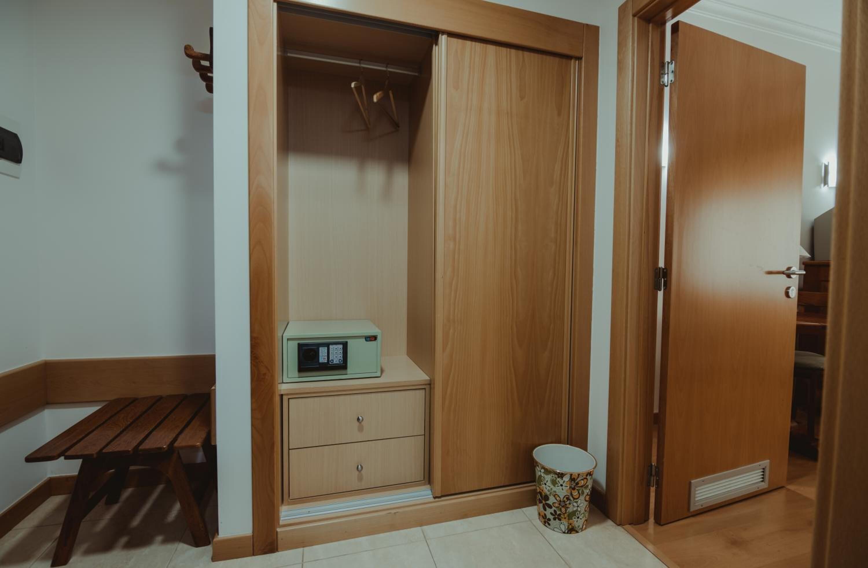 Una habitación con un armario de madera, una mesita con un radio y un cubo de basura.