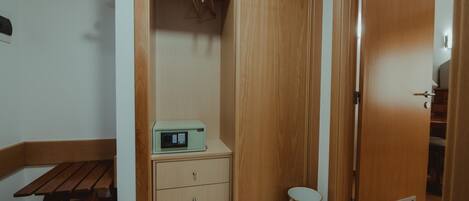 A room with a wooden wardrobe, a small table with a radio, and a trash bin.