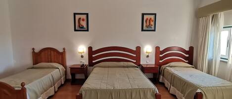 Habitación de hotel con tres camas individuales, cada una con cabecera de madera y una mesita de noche con lámpara.