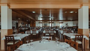 Un grand espace dédié à la salle à manger, avec plusieurs tables dressées, un lambris en bois au plafond et un téléviseur fixé au mur.