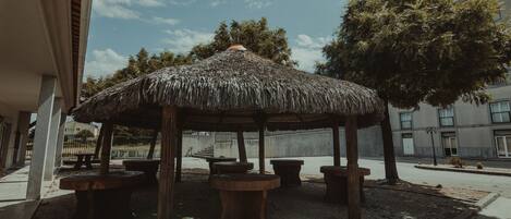An outdoor seating area with a thatched roof gazebo, stone tables, and benches.