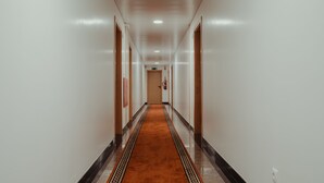 Un long couloir étroit, doté d’un tapis à motifs, de murs blancs et de portes en bois de chaque côté.
