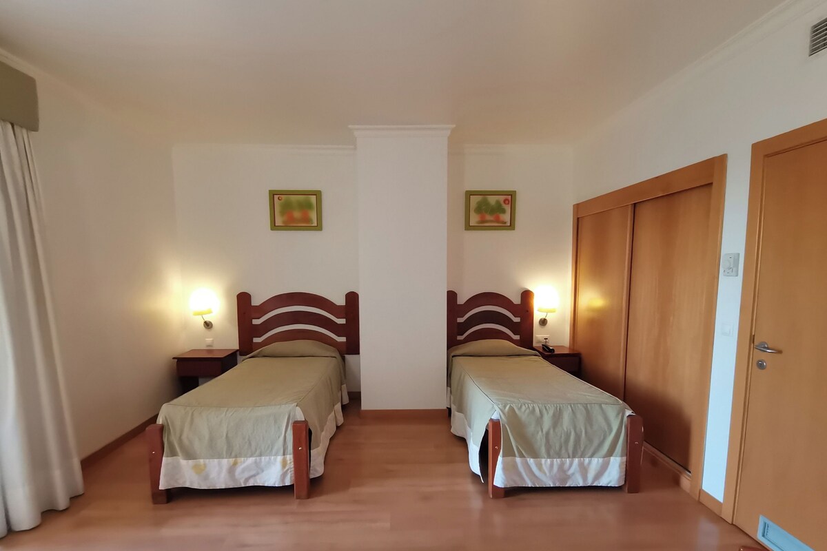 Een kamer met twee enkele bedden, houten hoofdborden, nachtkastjes met lampen en een houten garderobe.