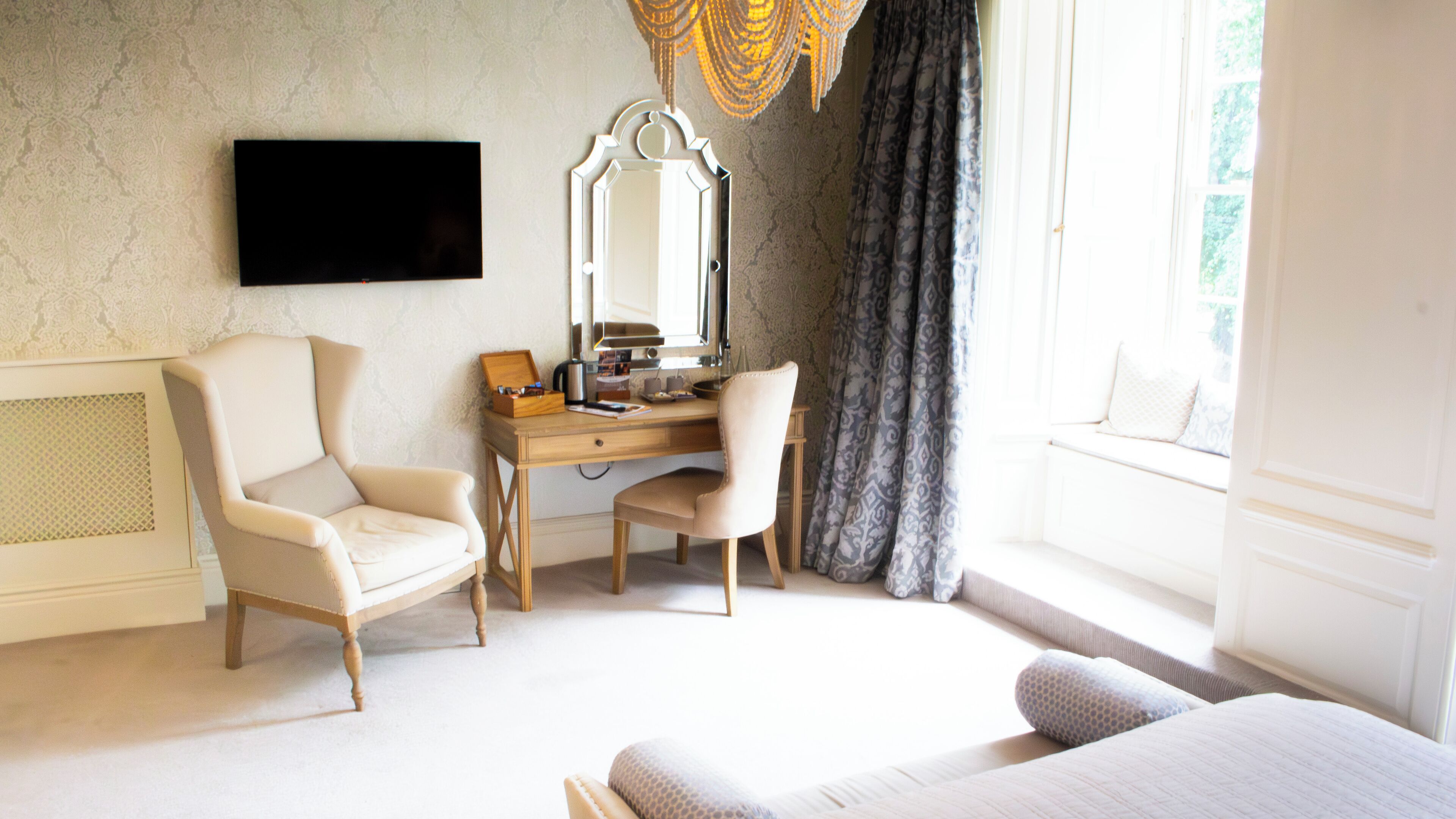 A hotel room with a bed, a desk with a chair, a television, a mirror, and a window with curtains.