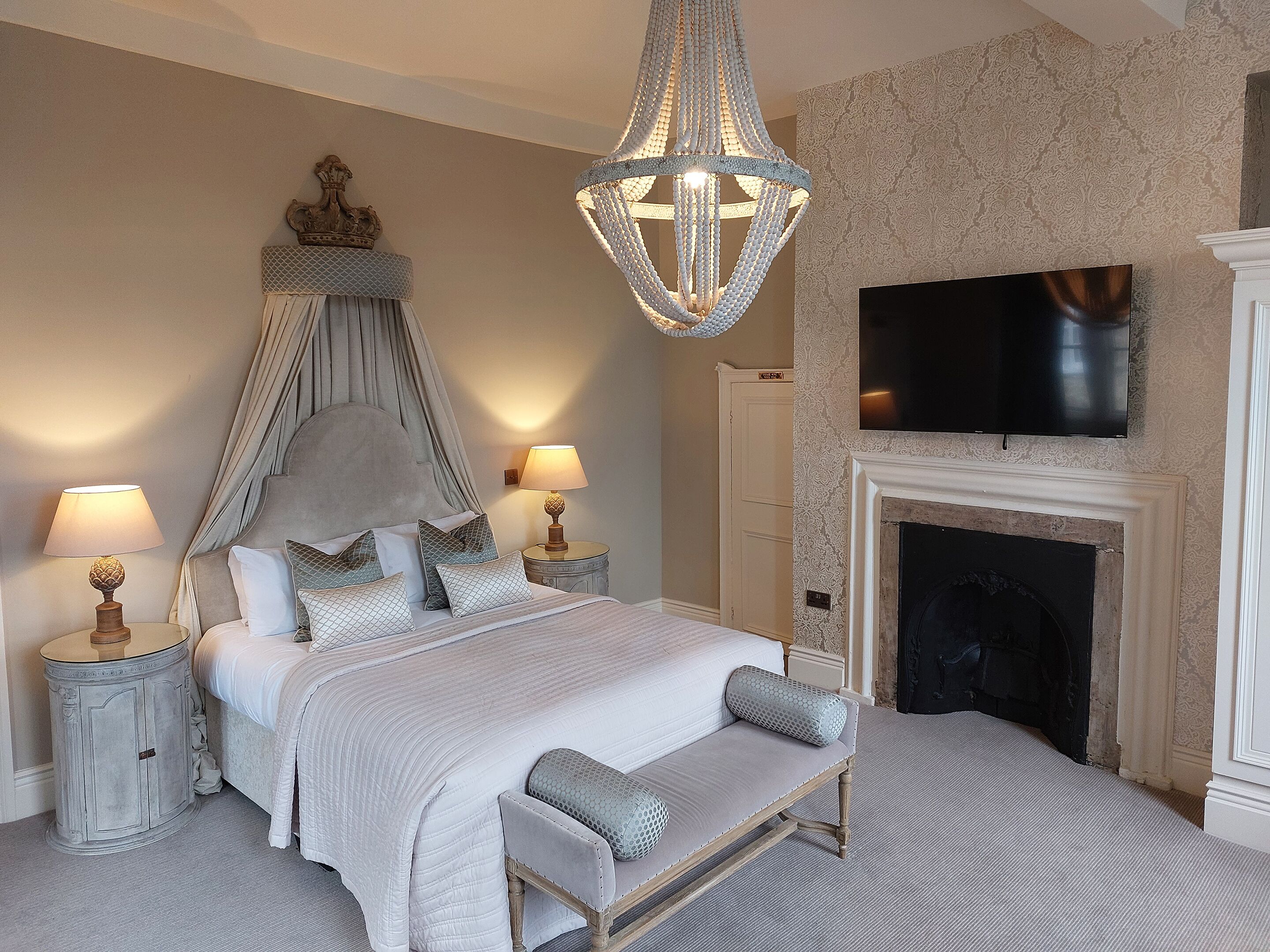 A bedroom with a four-poster bed, a chandelier, a television, and a fireplace.