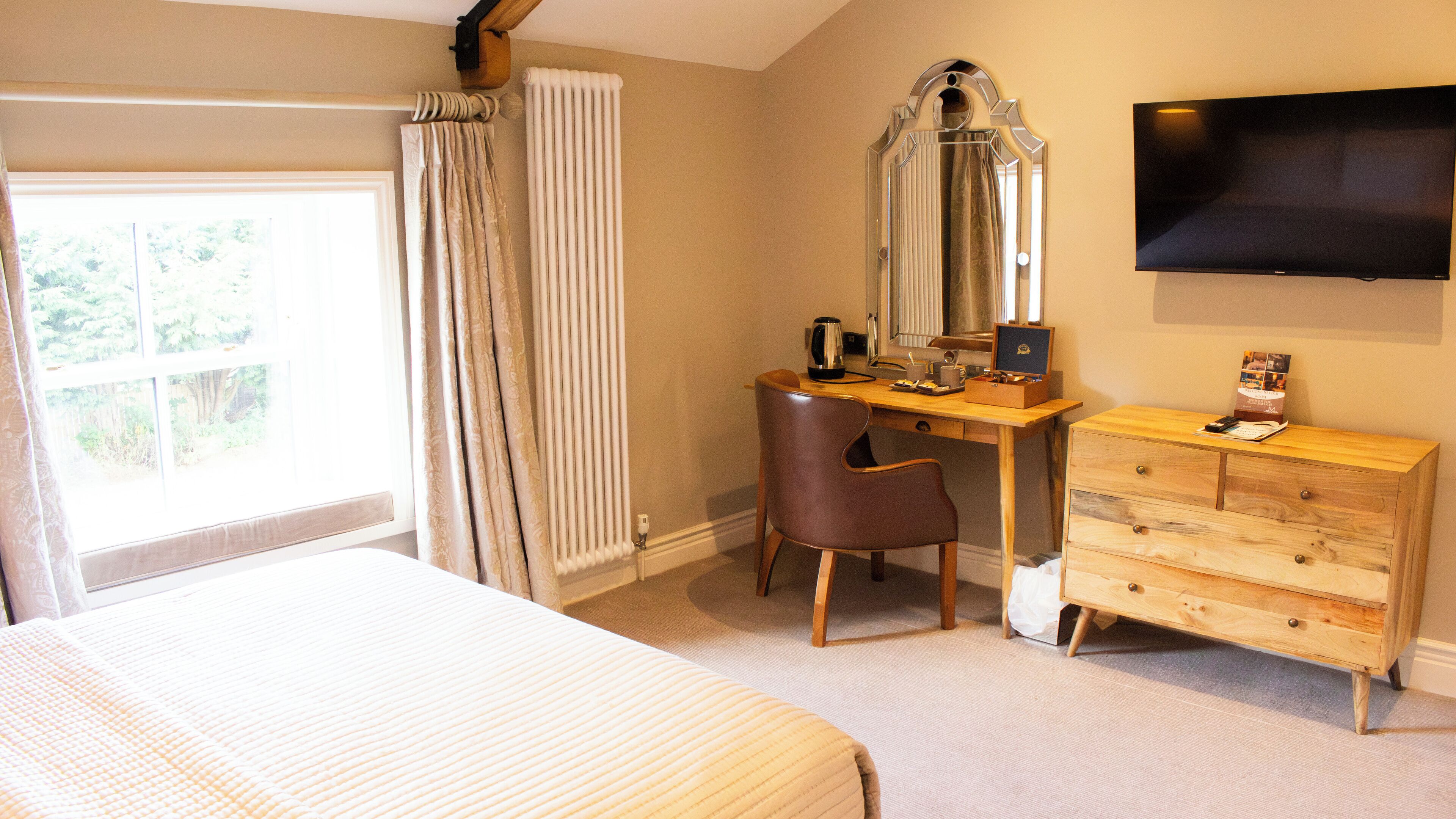 A bedroom with a bed, a desk, a chair, a dresser, a mirror, and a TV.