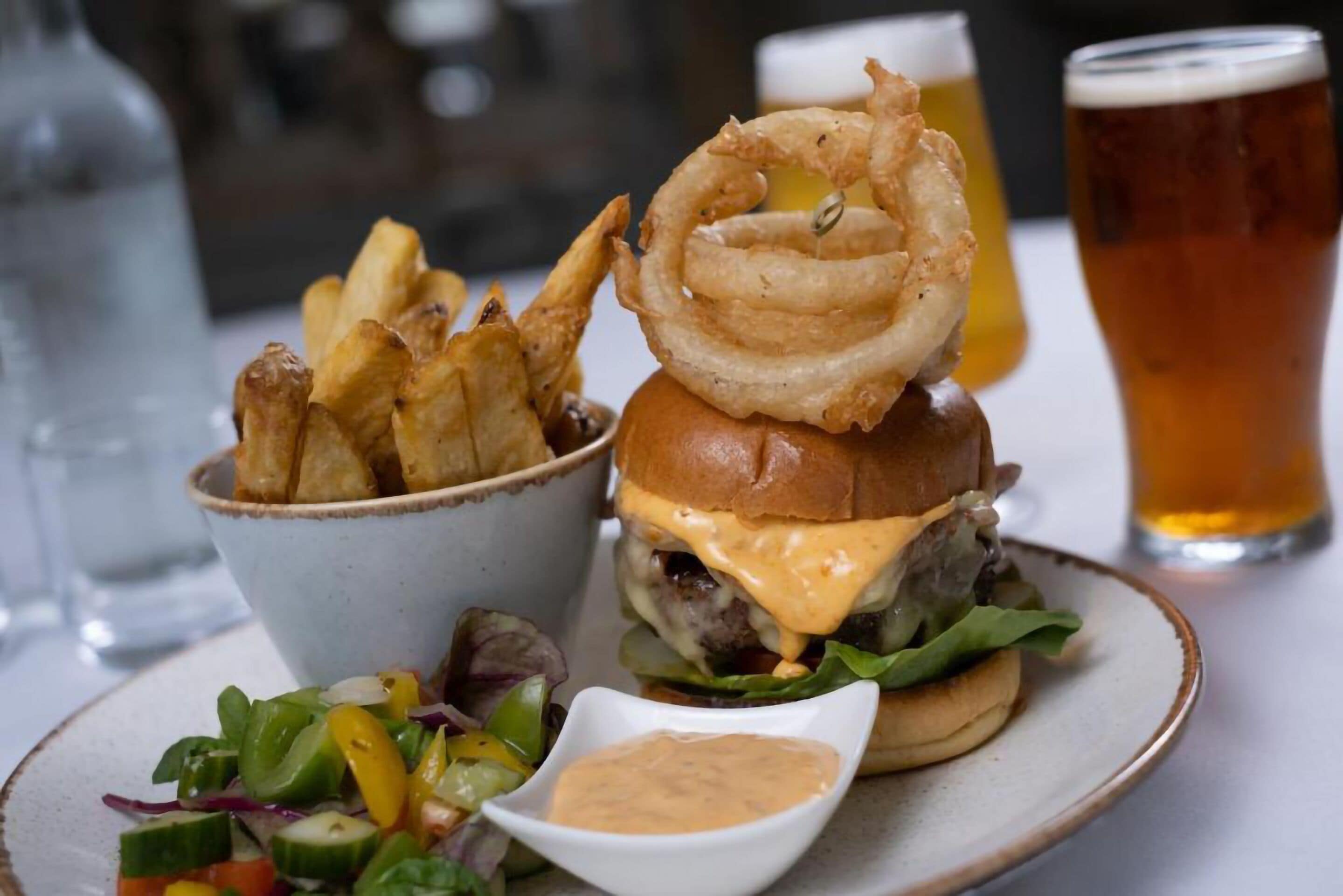 Ein Burger mit Brötchen, Käse, Salat und gebratener Zwiebel, dazu Pommes und ein Salat.