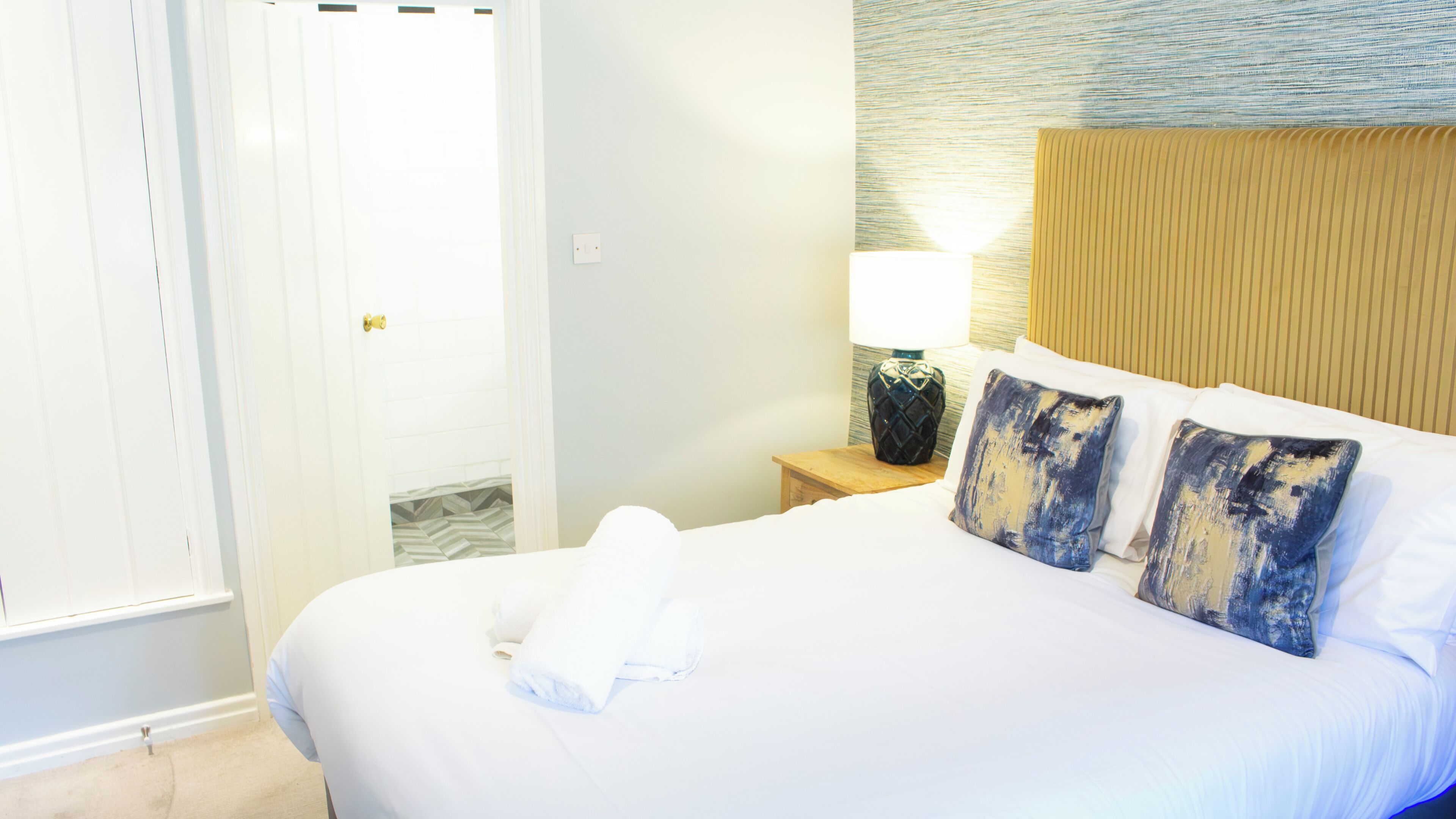 A hotel room with a neatly made bed, a bedside lamp, and a nightstand.