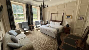 Quarto de hotel com uma cama grande, duas poltronas, um sofá, uma mesinha e uma cadeira de madeira.