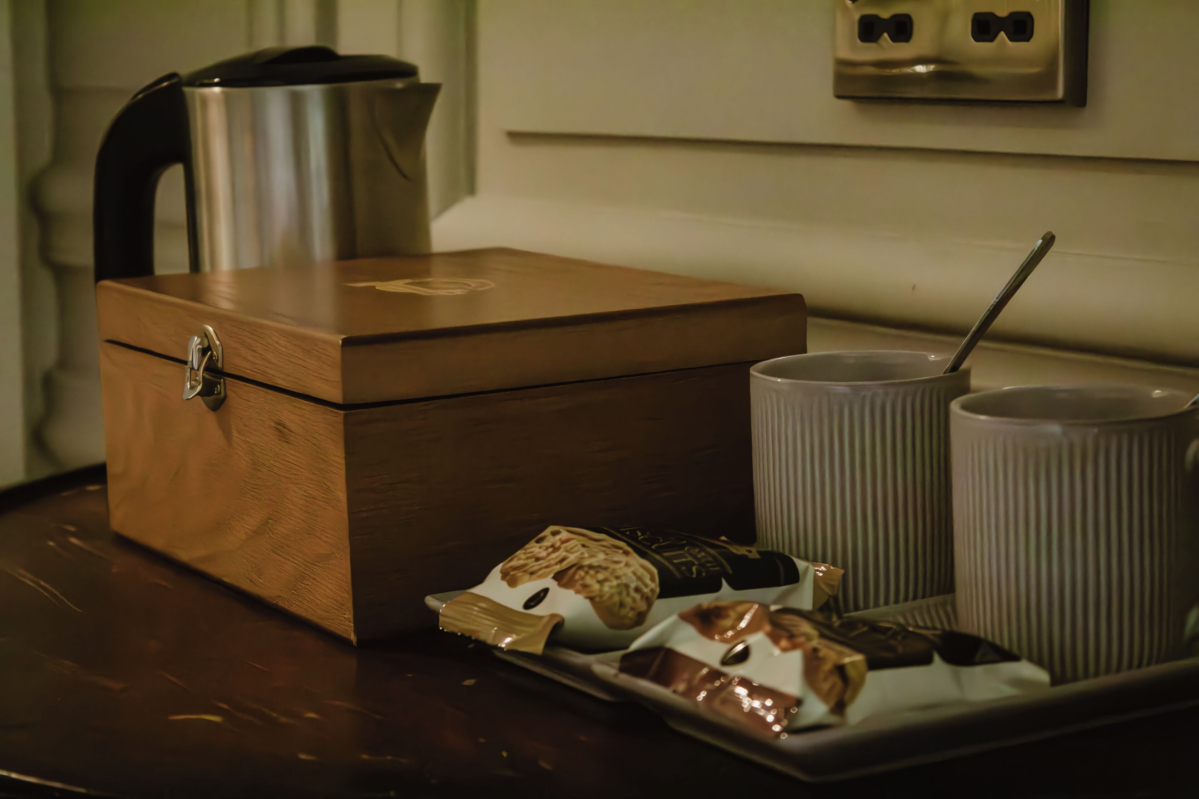 A wooden box with a lock, a kettle, two cups with straws, and a tray with food items.