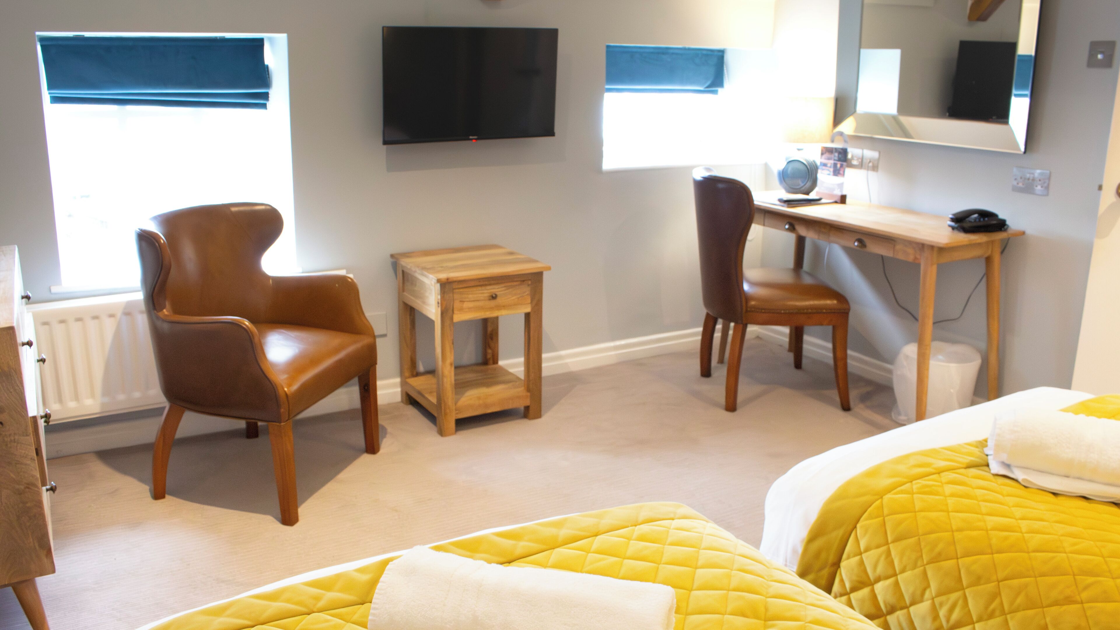A hotel room with a bed, two chairs, a desk, a television, and a window.
