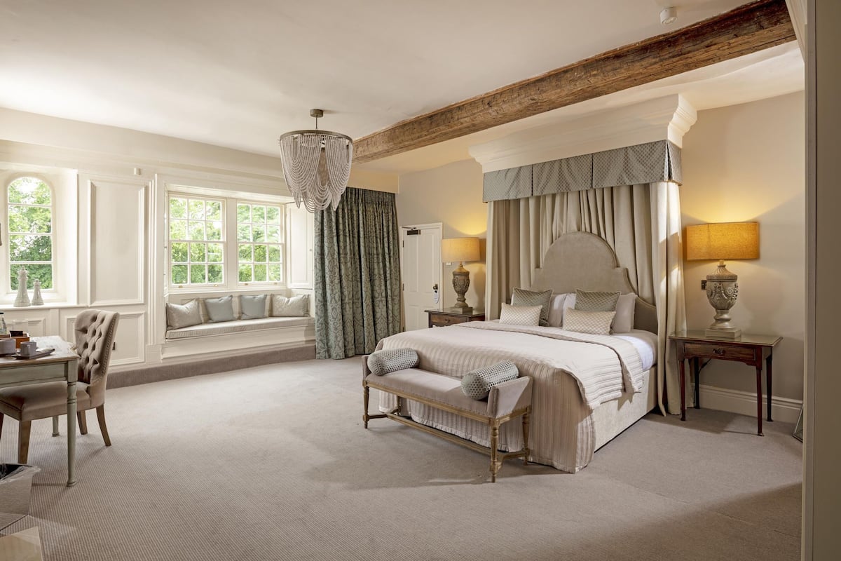 A spacious bedroom with a large bed, a bench, a desk, and a window seat.