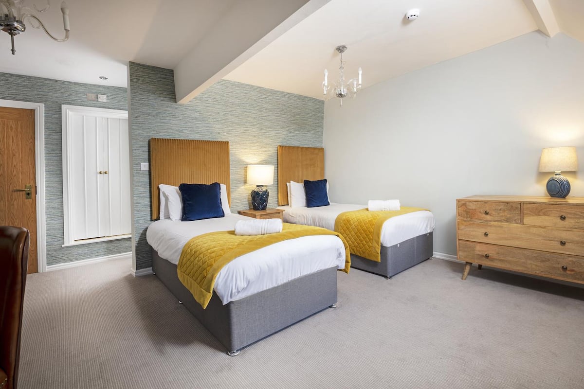 A hotel room with two beds, a wooden dresser, and a chandelier.