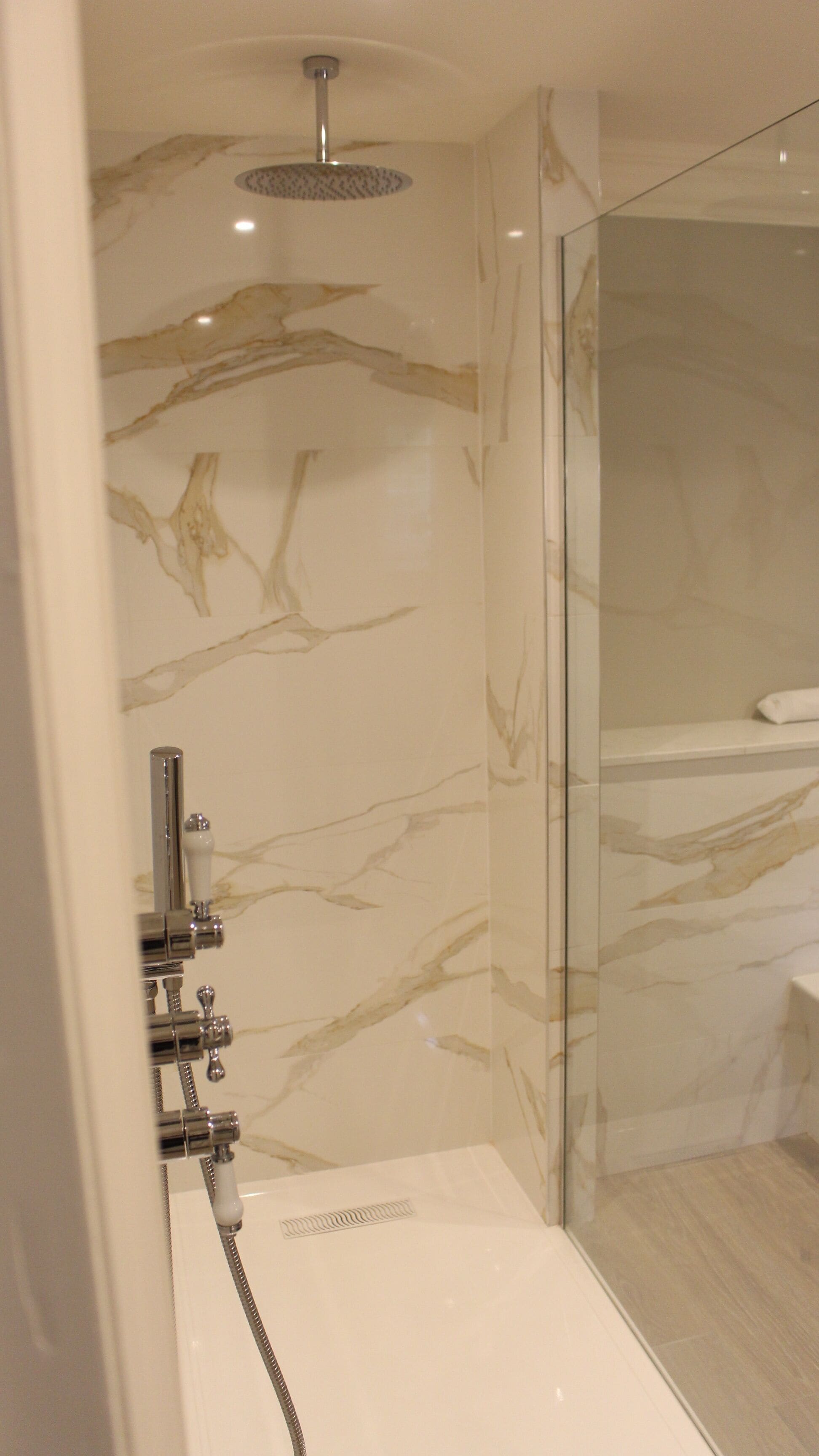 A modern bathroom with a glass shower enclosure, marble walls, and a chrome showerhead.