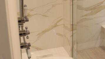 A modern bathroom with a glass shower enclosure, marble walls, and a chrome showerhead.