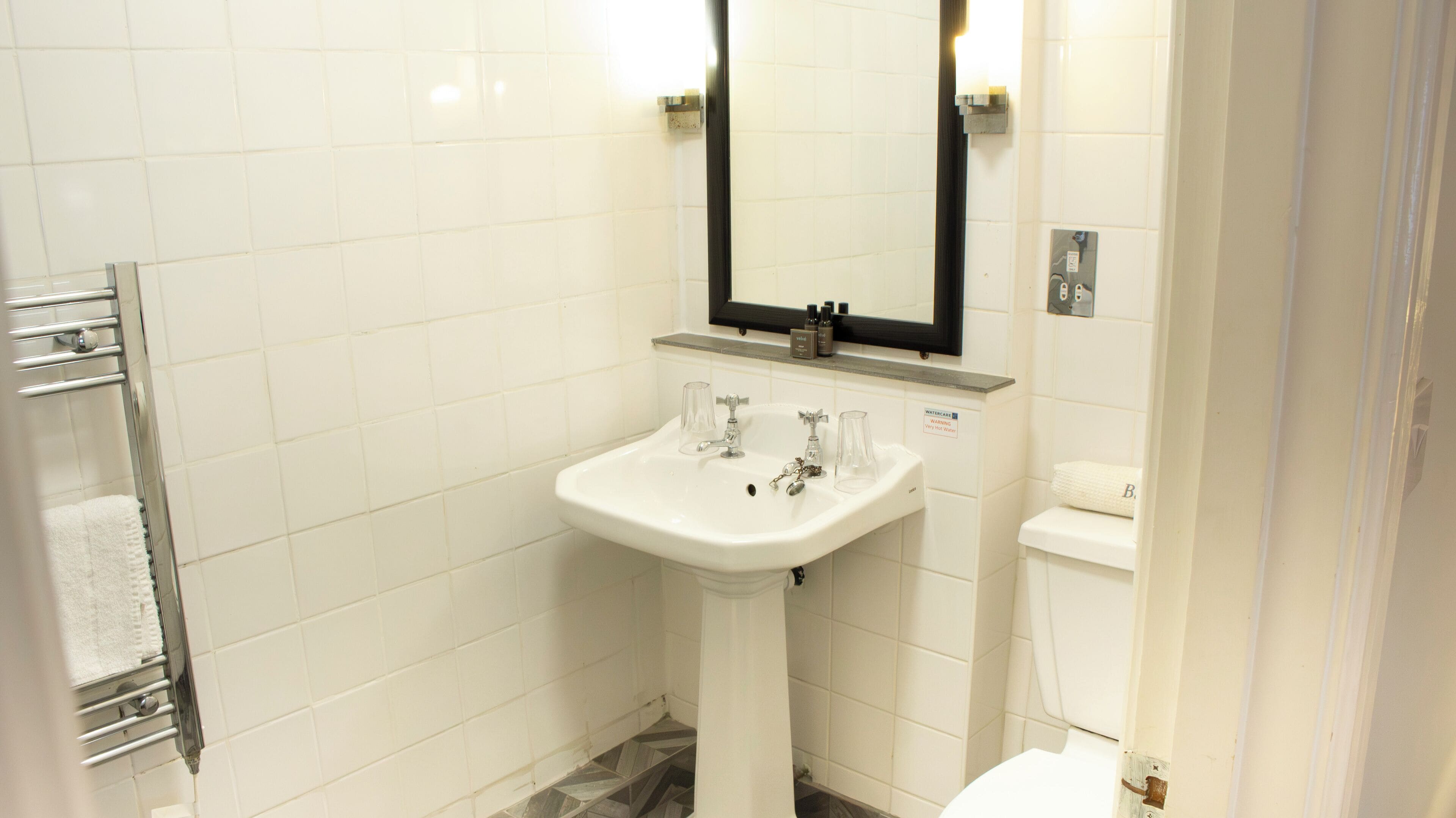 Casa de banho com lavatório branco, espelho e suporte para toalhas.