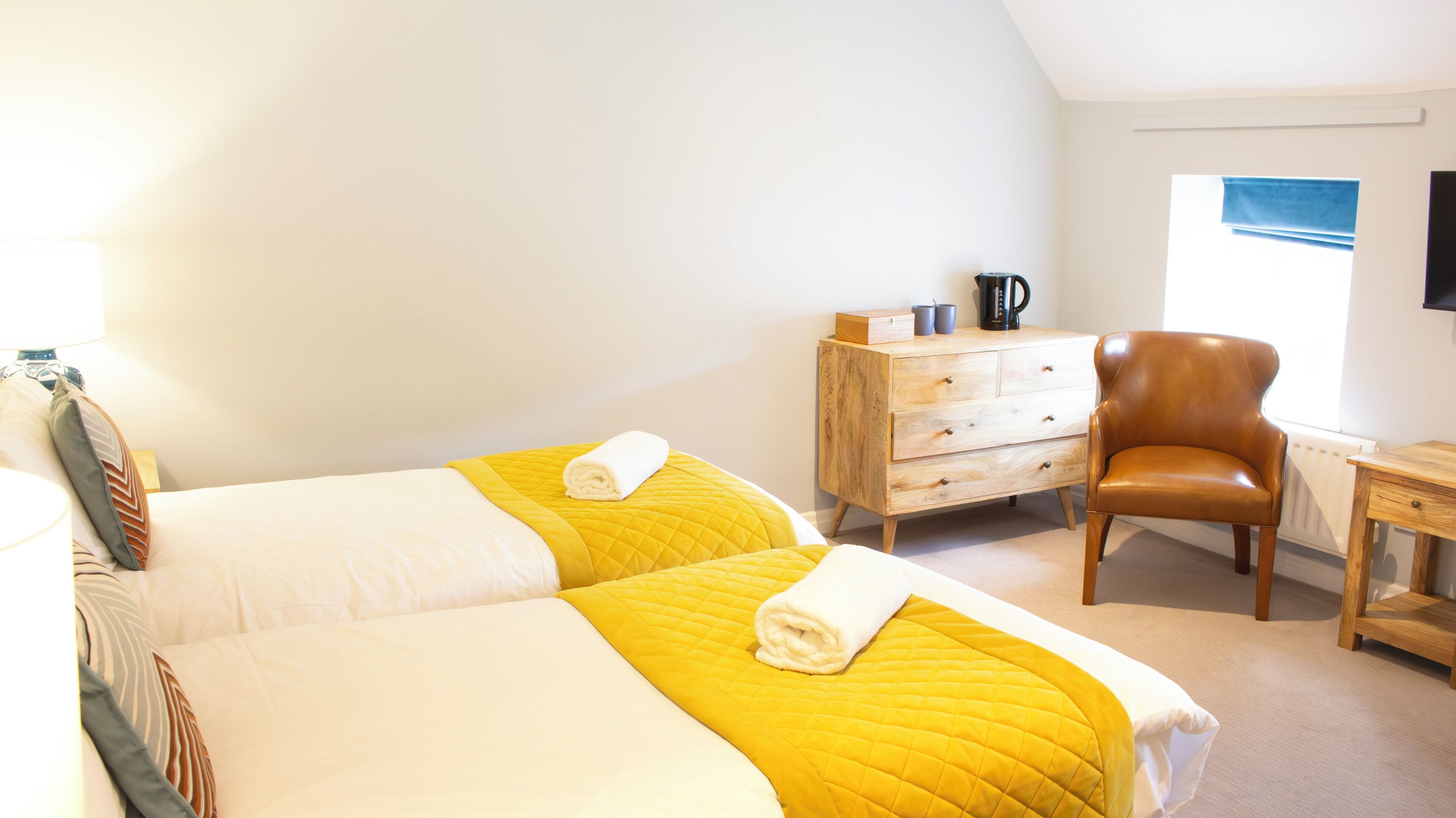 Habitación de hotel con dos camas, un aparador de madera, un sillón de cuero y una mesita.