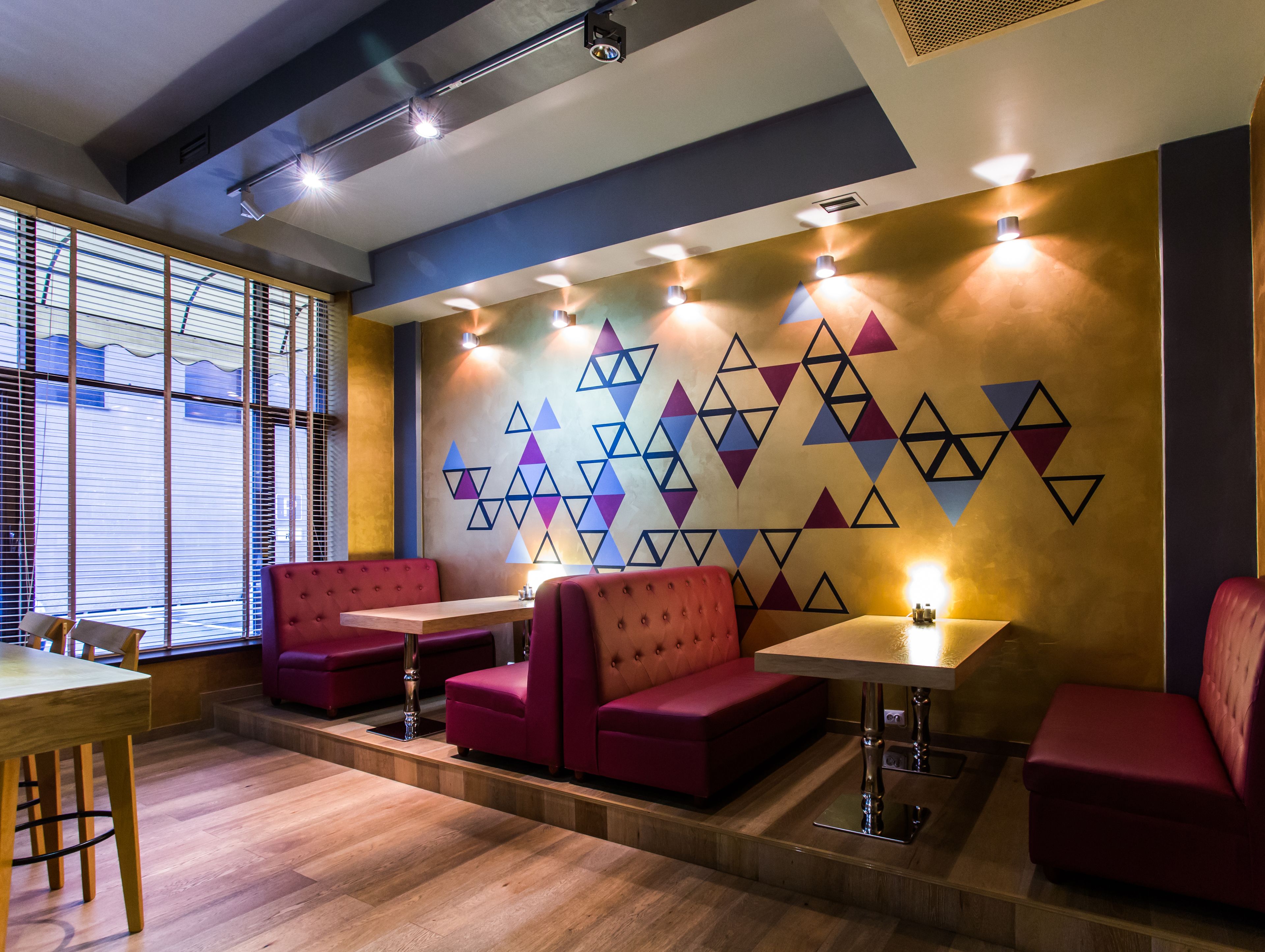 A modern restaurant interior with red booths, wooden tables, and a geometric wall design.