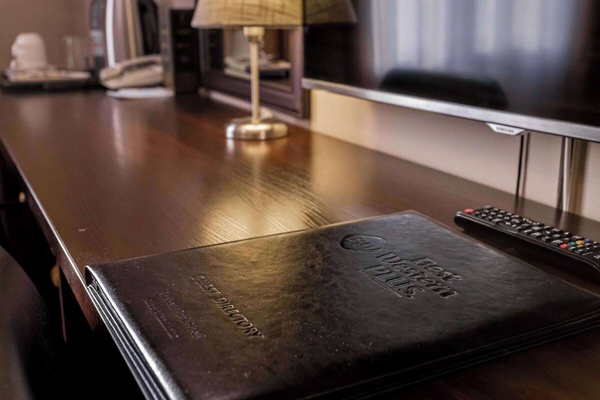 A wooden desk with a leather-bound book titled "Best Western" and a remote control.