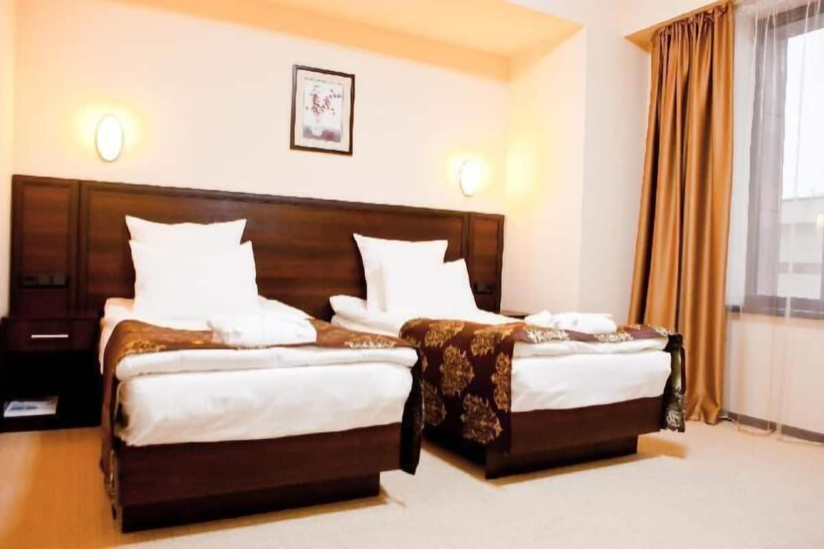 A hotel room with two beds, a nightstand, a framed picture on the wall, and a window with curtains.