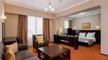Hotelkamer met een bank, fauteuil, salontafel, bureau, televisie en een bed met hoofdeinde.