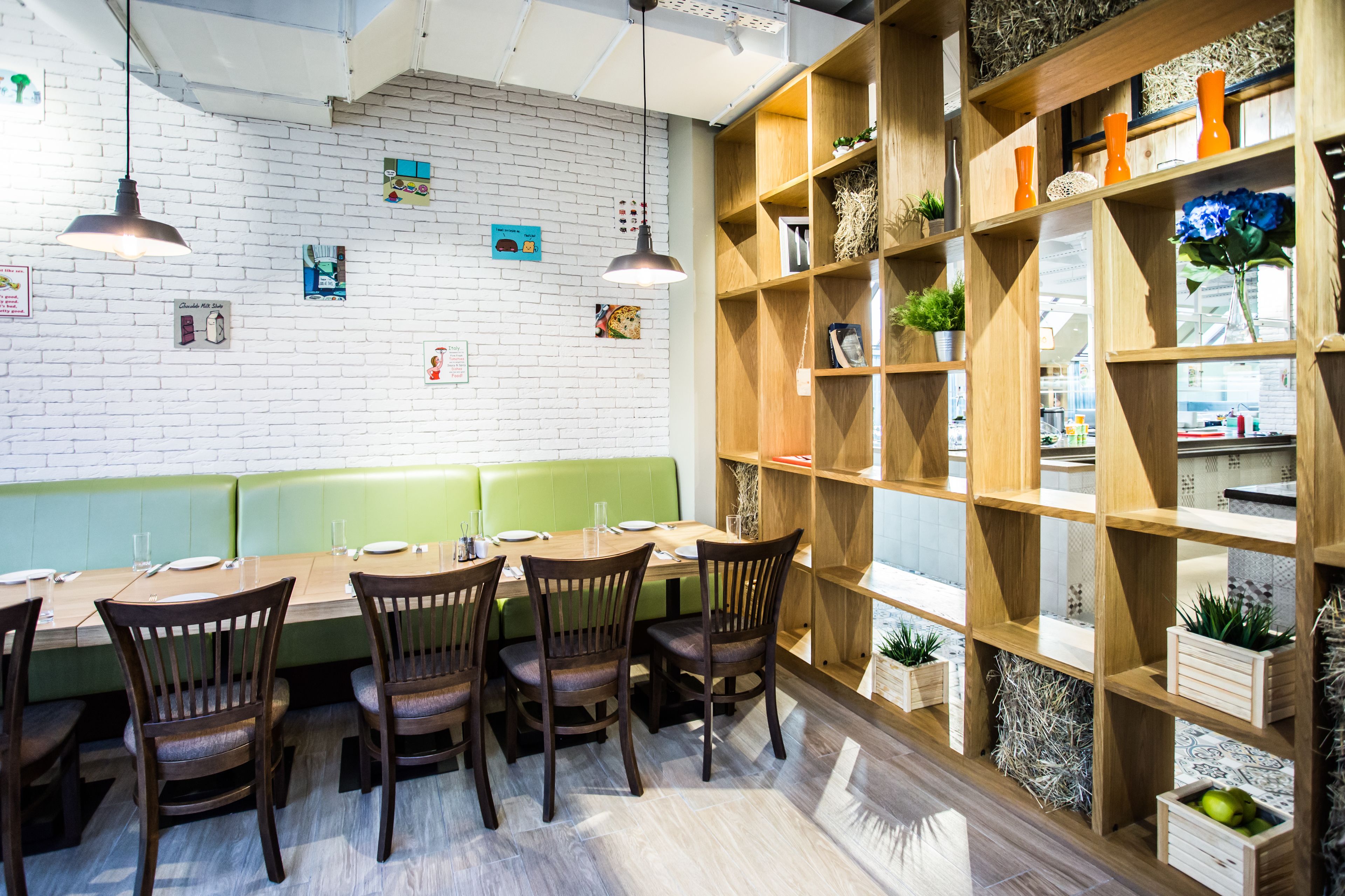 A restaurant with a long wooden table, green cushioned booth, and wooden shelves with plants and decorative items.