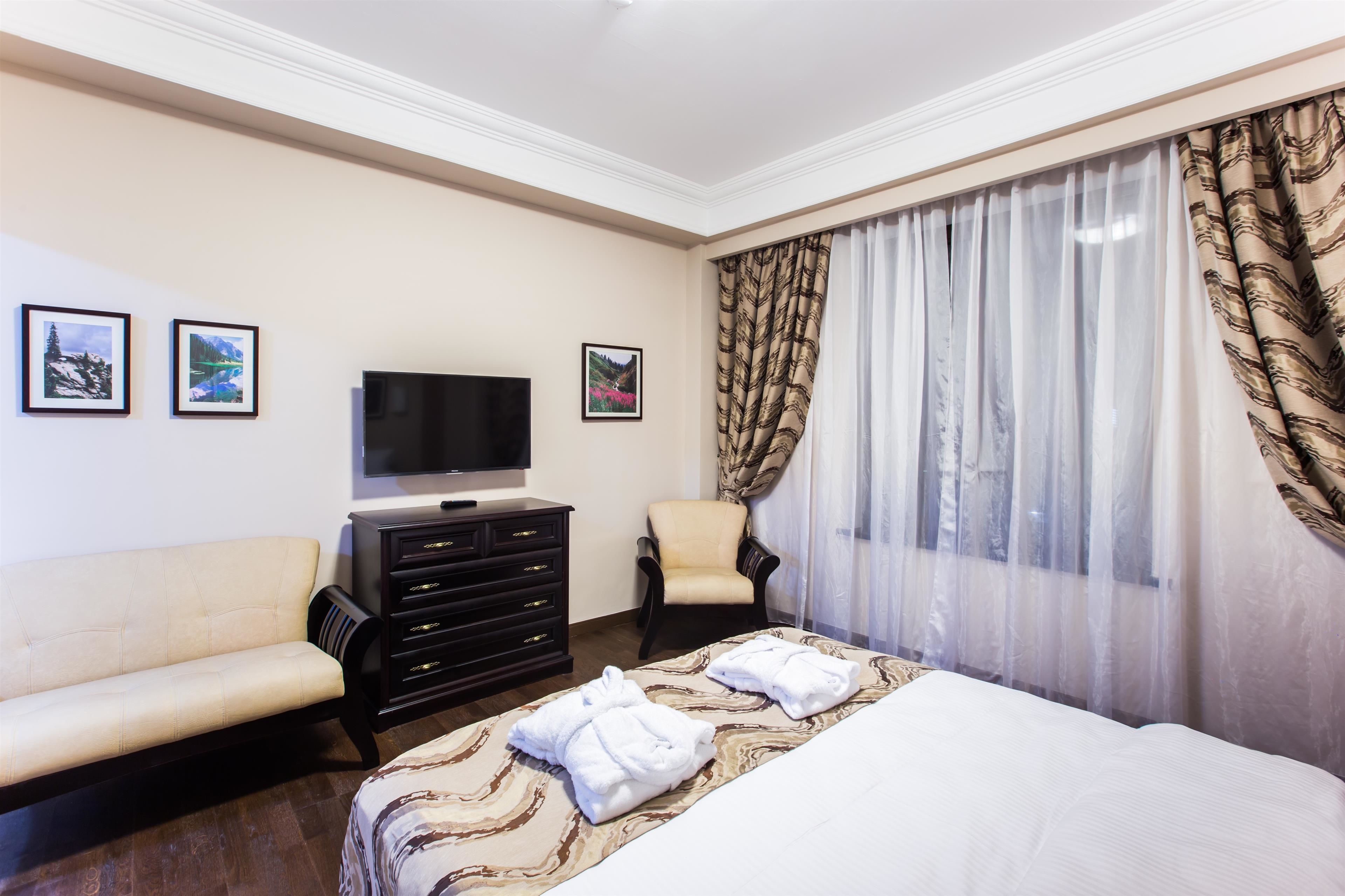 A hotel room with a bed, a TV, a sofa, a chair, and a dresser.