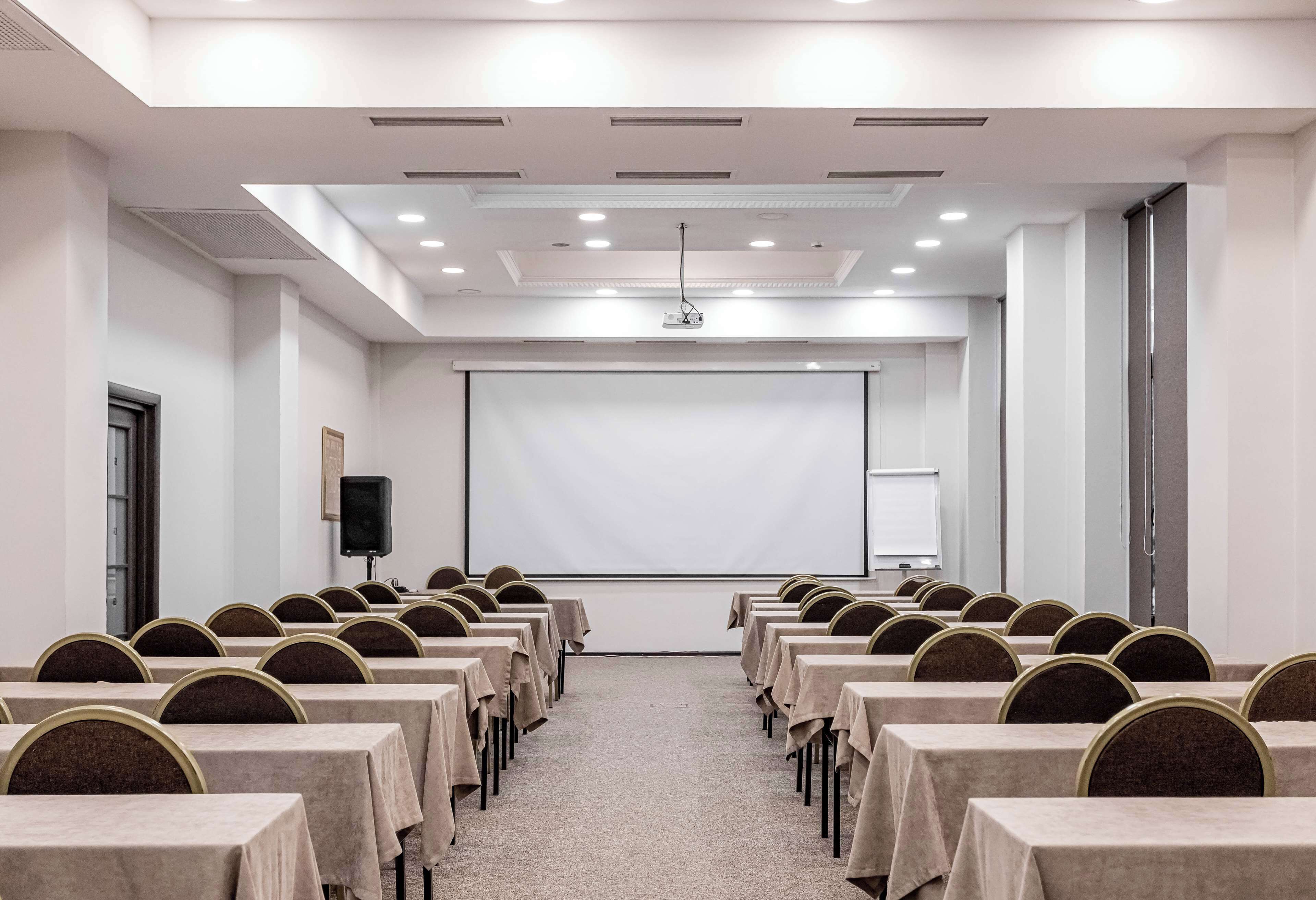 A conference room with rows of tables and chairs, a projector screen, and a whiteboard.