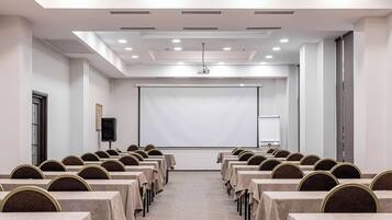 A conference room with rows of tables and chairs, a projector screen, and a whiteboard.