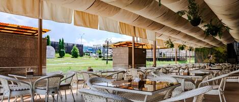 An outdoor seating area with wicker chairs and tables, a covered roof, and hanging plants.