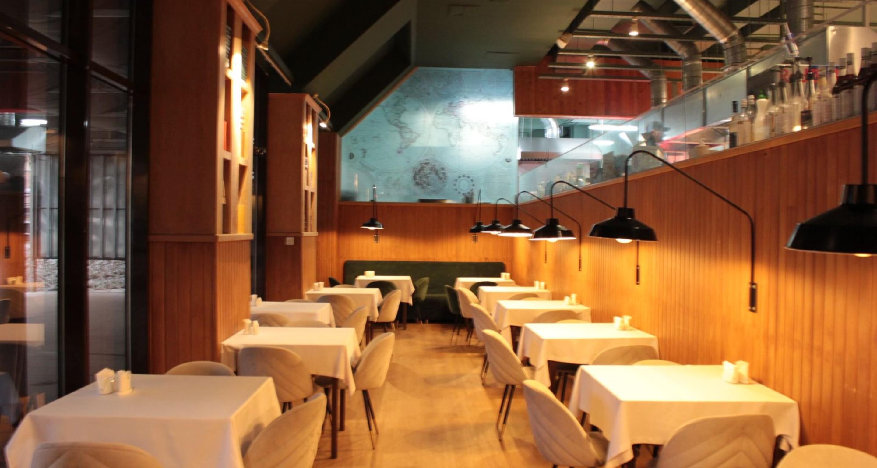 A restaurant with multiple tables and chairs, wooden walls, and hanging pendant lights.