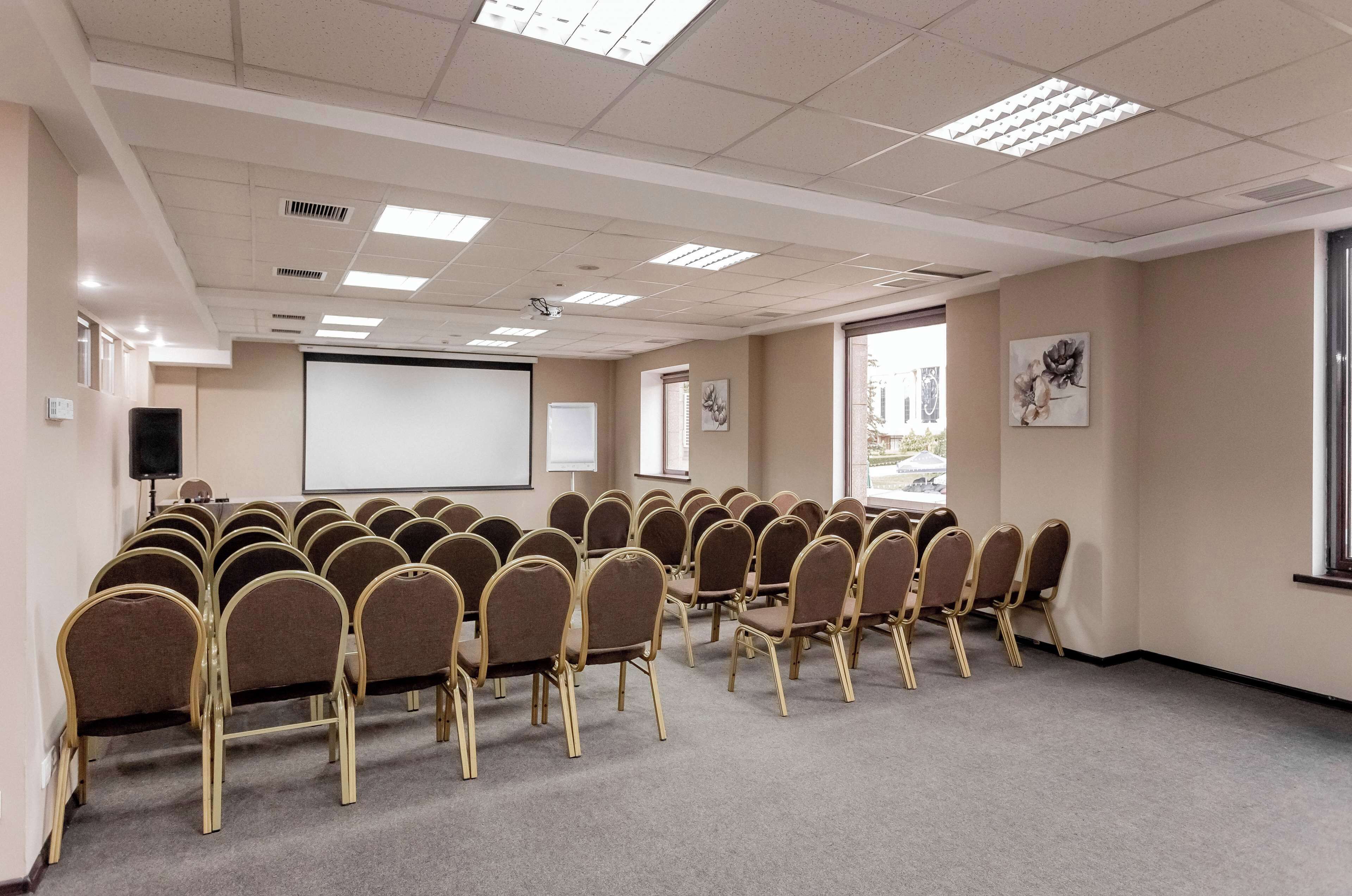 Uma sala de conferência com fileiras de cadeiras, uma tela de projetor e um quadro branco.