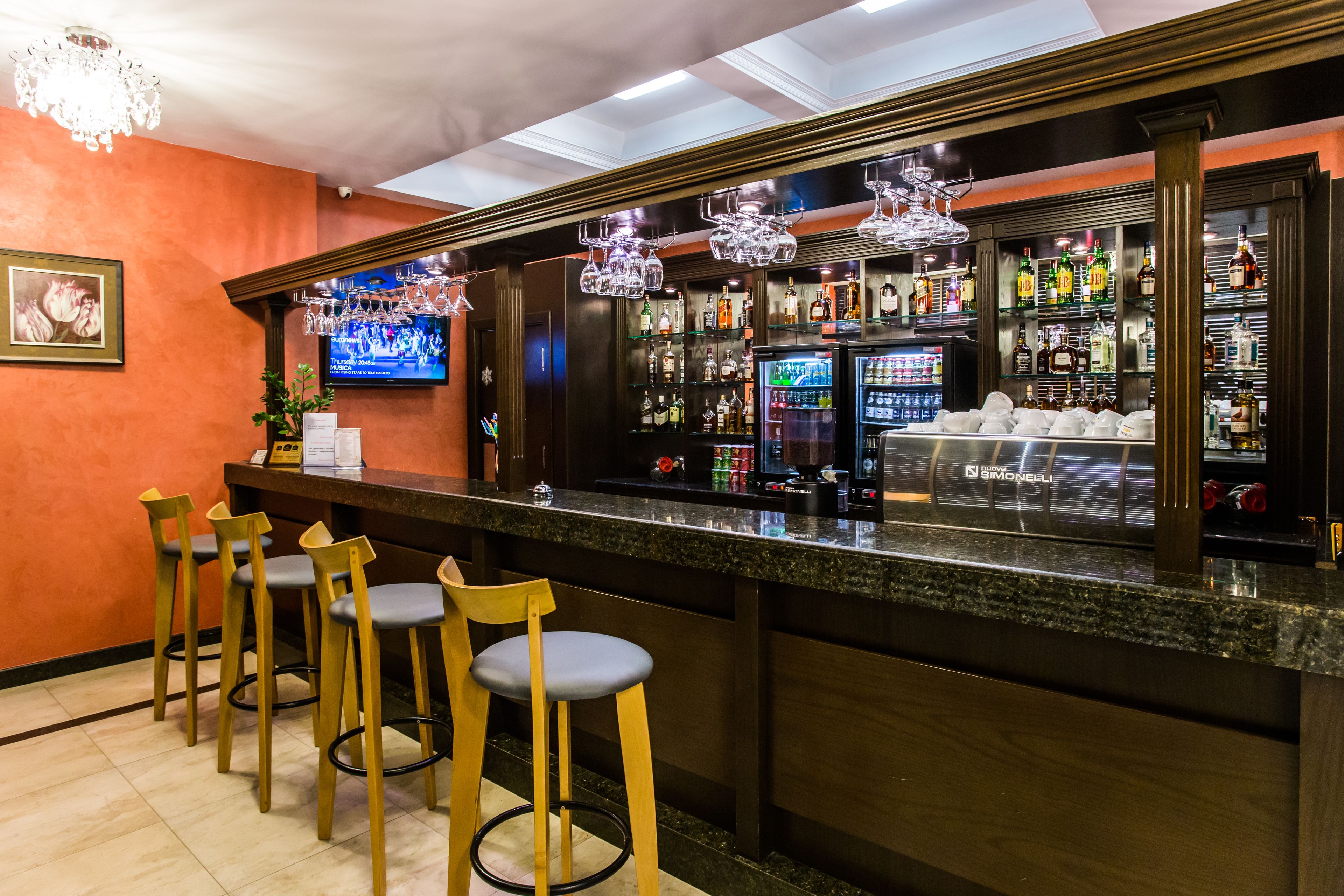 A bar area with a counter, stools, a television, and a variety of bottles and glasses.