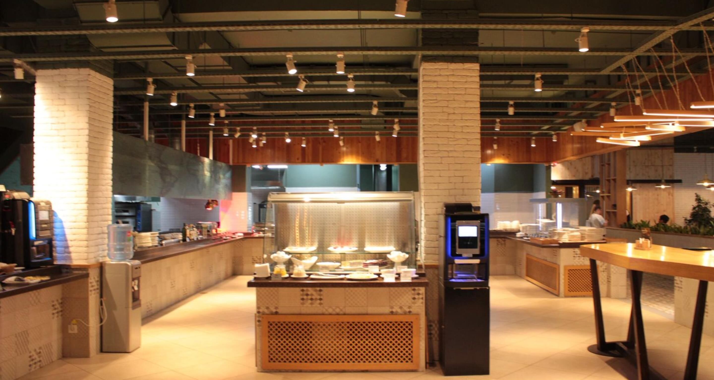 Un restaurant moderne avec un comptoir central, un distributeur de boissons en libre-service et un espace repas avec des tables.