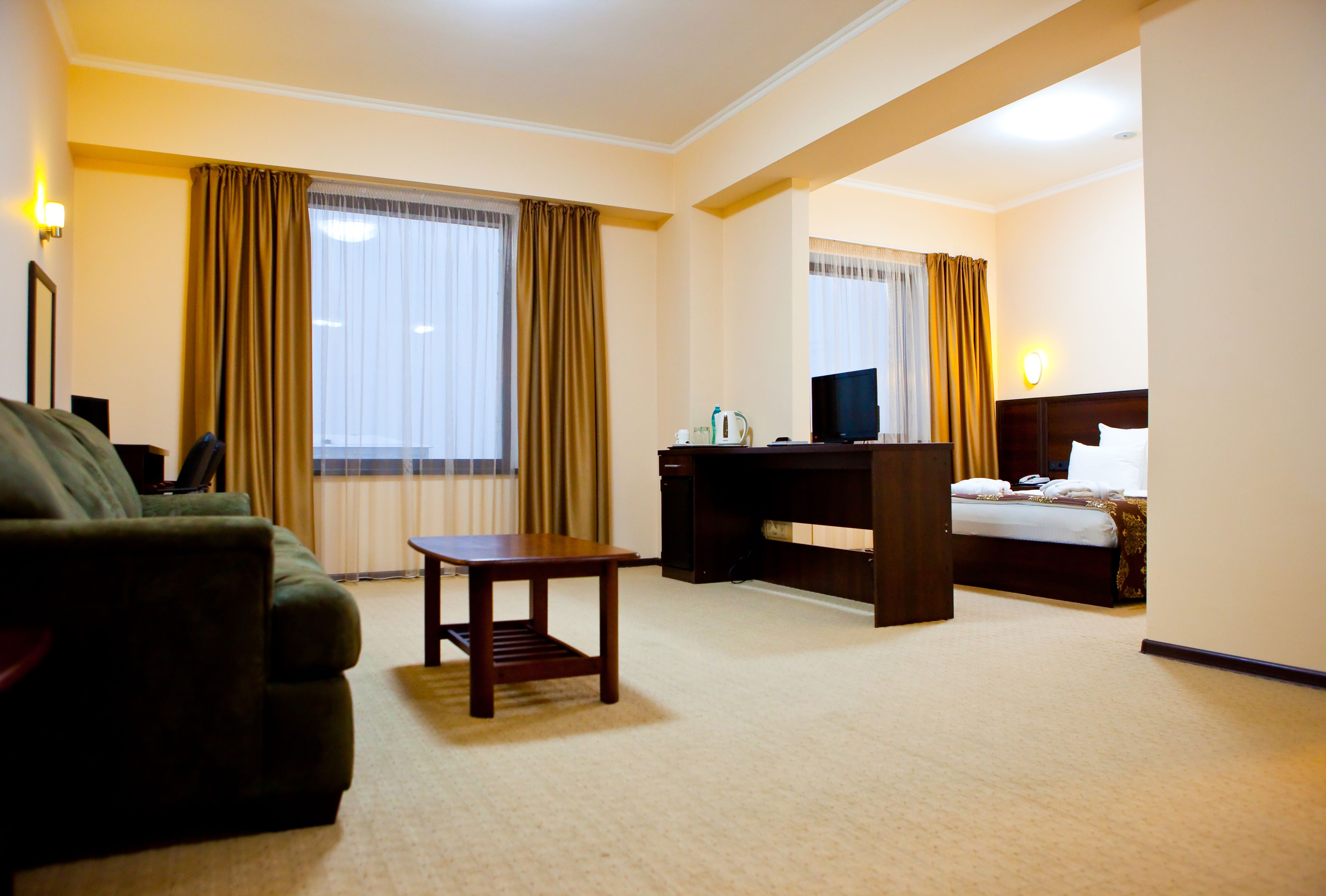 Een hotelkamer met een bank, een tafeltje, een bureau met een computer, een bed en een televisie.