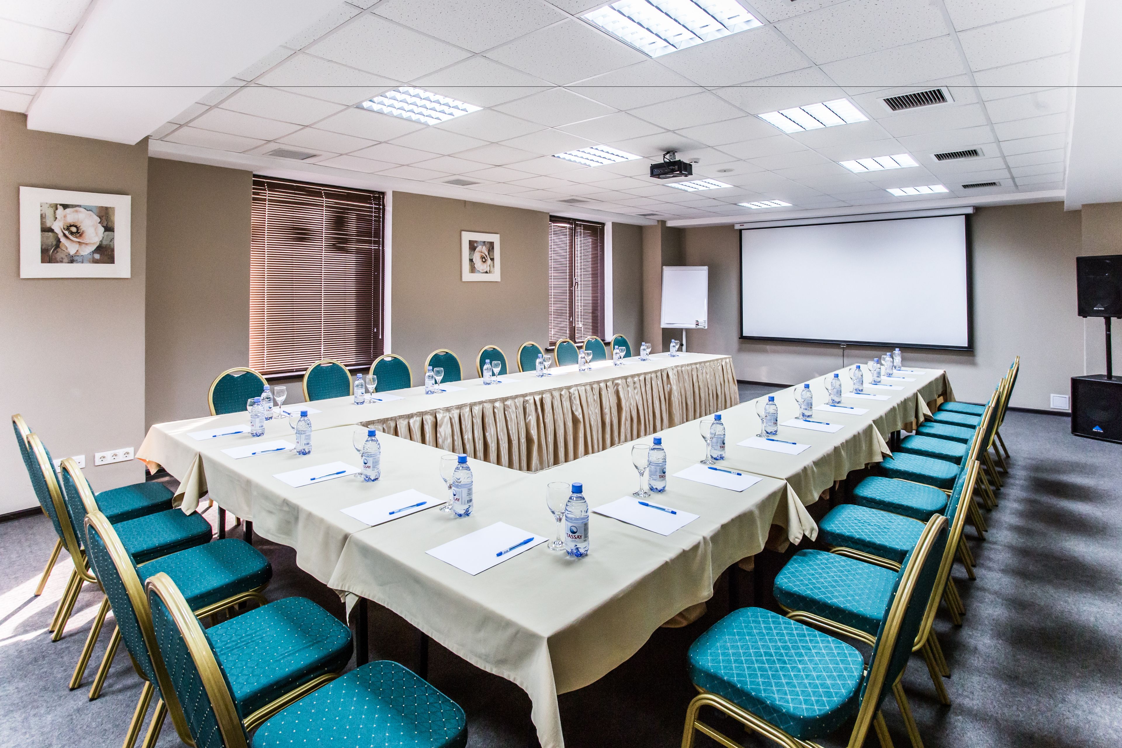Un salón de conferencias con una larga mesa, sillas color turquesa y una pantalla de proyector.