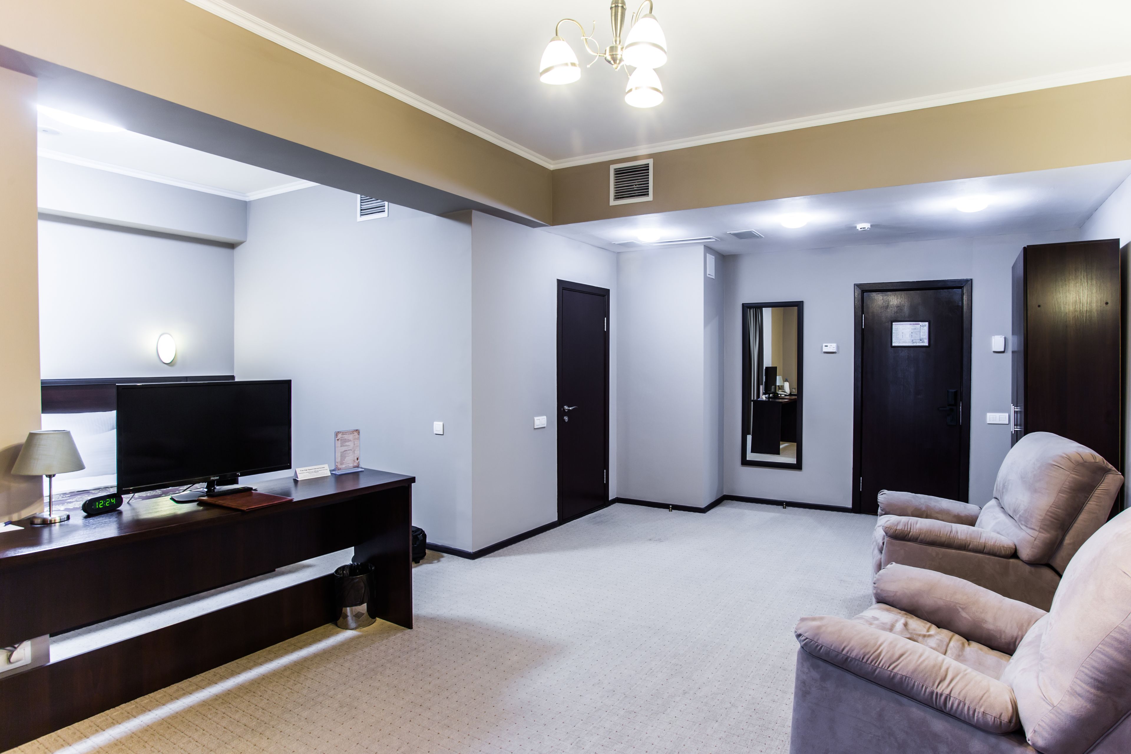 A hotel room with a dark wooden desk, a flat-screen TV, a lamp, a sofa, and a large mirror.