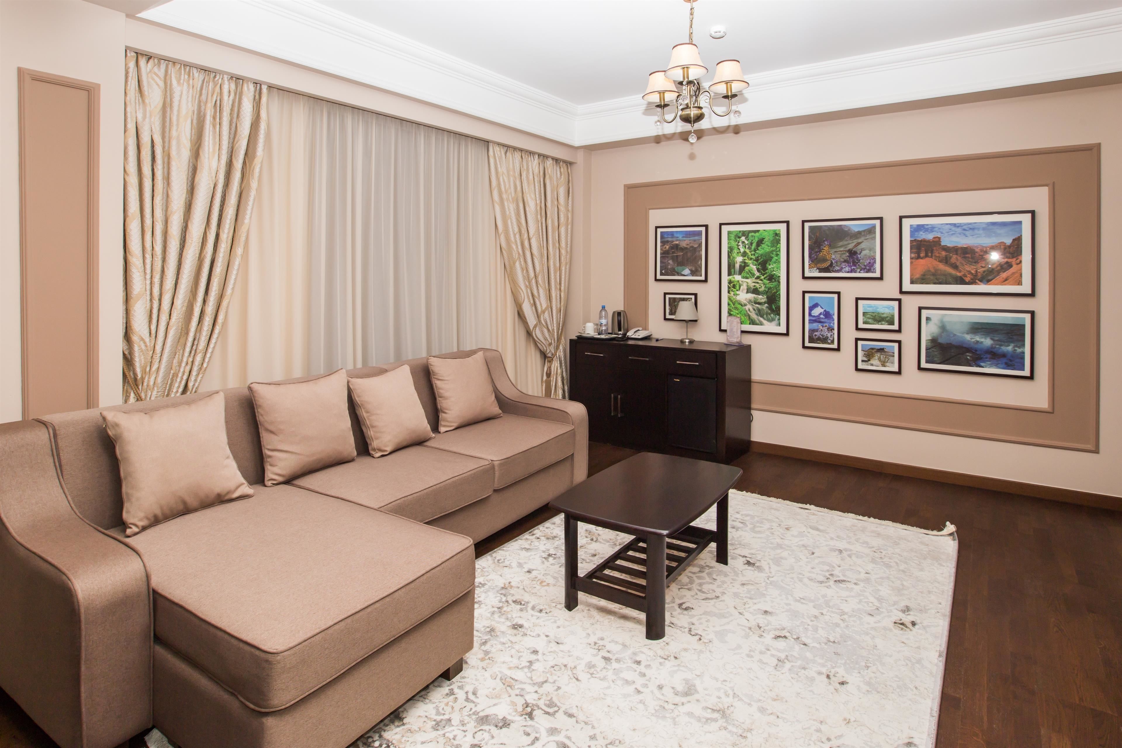 A living room with a beige sofa, a coffee table, and a cabinet. There are framed pictures on the wall.