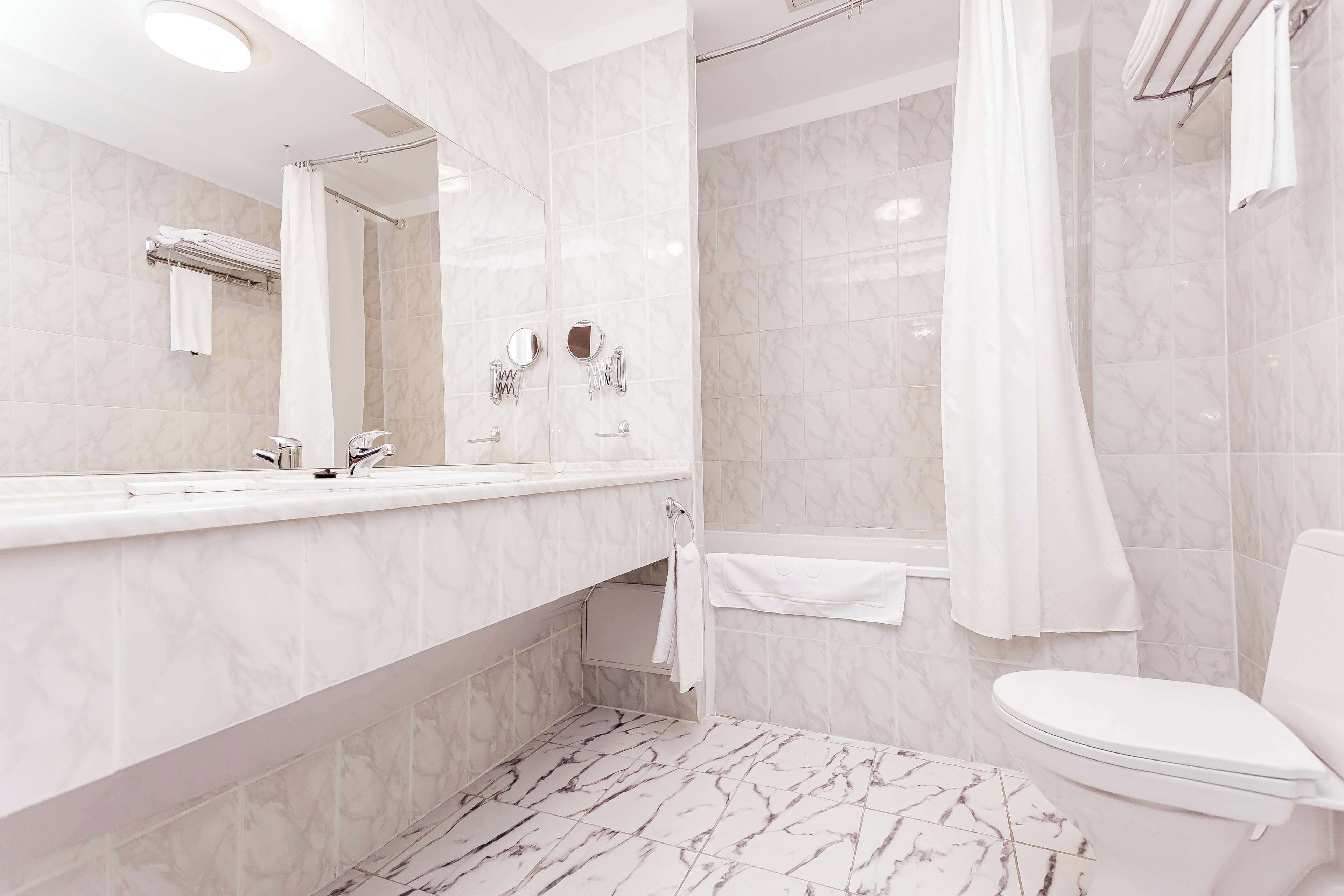 Een moderne badkamer met een marmeren vloer, een grote spiegel, een wit toilet en een douchehoek.