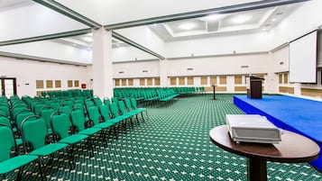 A conference room with rows of green chairs, a blue stage, and a projector on a table.