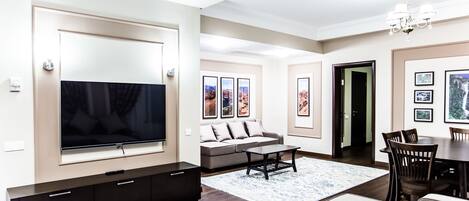 Een moderne woonkamer met een grote flatscreen-televisie, een bank, een salontafel en een eethoek met stoelen.