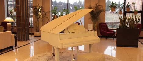 Un piano de cola en un vestíbulo amplio con piso de mármol, sillas rojas y plantas en macetas.