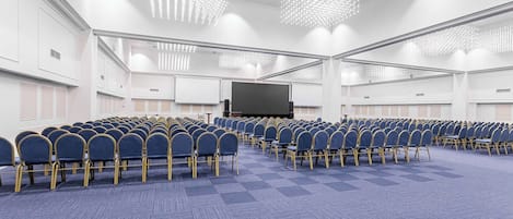 A conference room with rows of blue chairs, a large screen, and modern chandeliers.